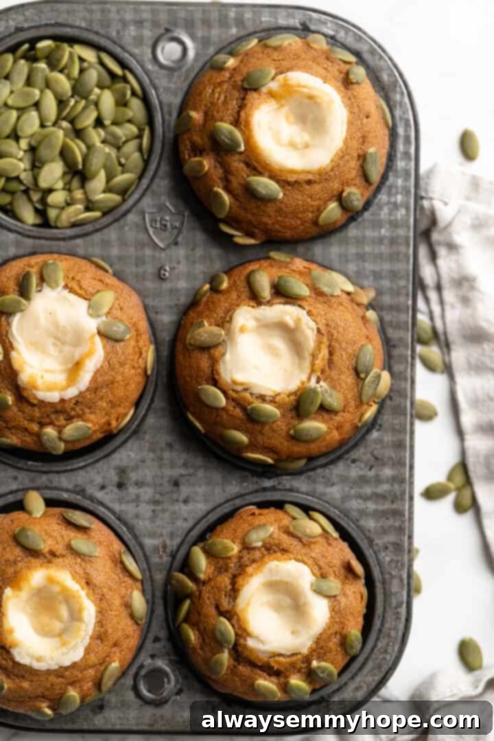 These vegan pumpkin cream cheese muffins pair the cozy flavour of pumpkin with a sweet-and-tangy cream cheese filling with delicious results! Overhead view of pumpkin cream cheese muffins in a pan, topped with pepitas before baking.