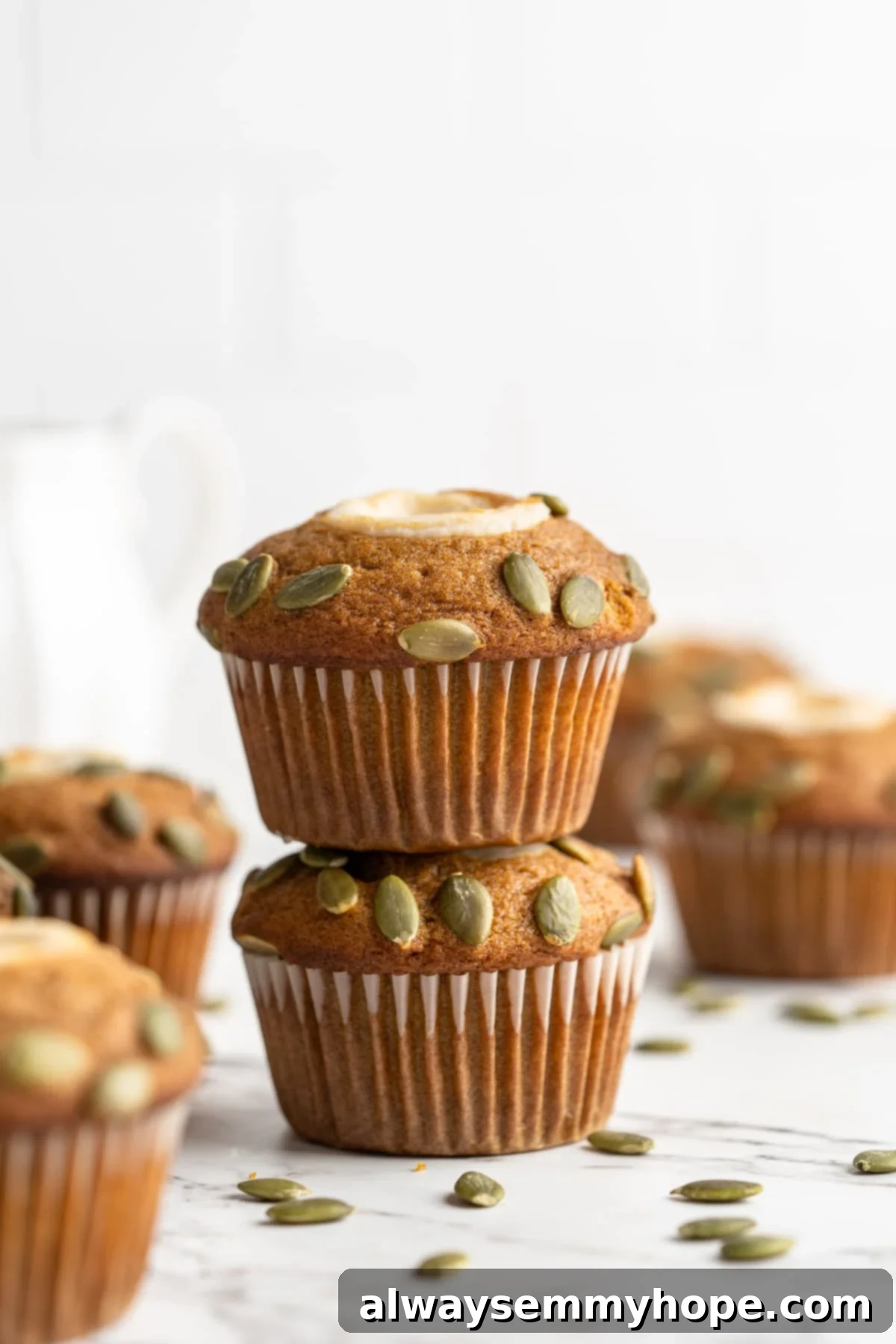 These vegan pumpkin cream cheese muffins pair the cozy flavour of pumpkin with a sweet-and-tangy cream cheese filling with delicious results! Two perfectly baked pumpkin cream cheese muffins stacked on a countertop, showing their fluffy texture and creamy filling.