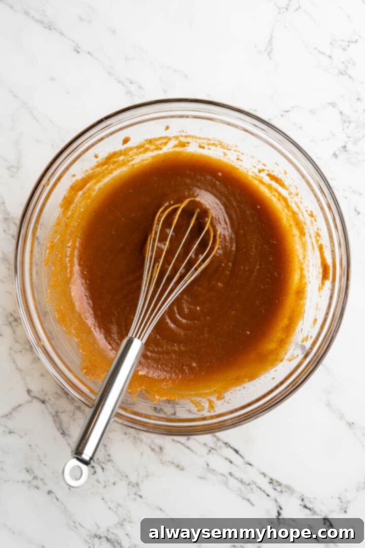 These vegan pumpkin cream cheese muffins pair the cozy flavour of pumpkin with a sweet-and-tangy cream cheese filling with delicious results! Wet ingredients for pumpkin cream cheese muffins in a glass bowl, being whisked to combine.