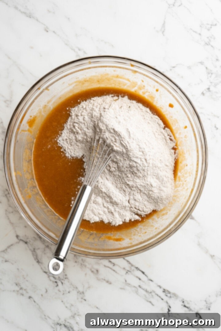 These vegan pumpkin cream cheese muffins pair the cozy flavour of pumpkin with a sweet-and-tangy cream cheese filling with delicious results! Overhead view of dry ingredients being gently folded into the wet ingredients for pumpkin cream cheese muffins.