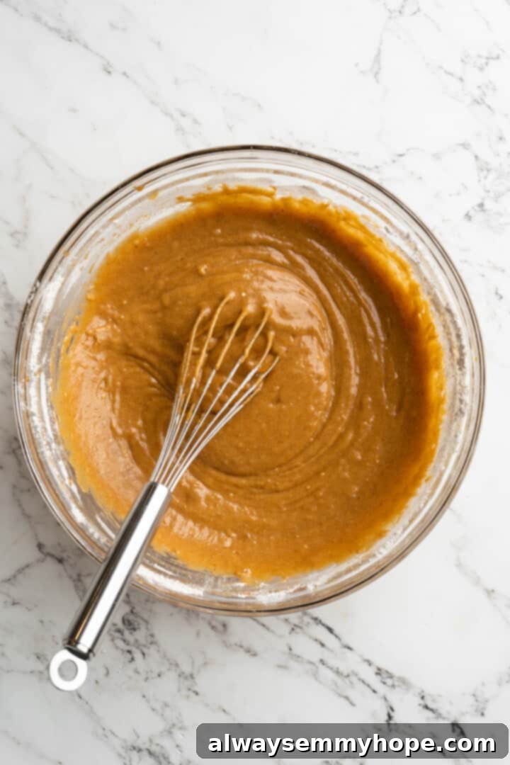 These vegan pumpkin cream cheese muffins pair the cozy flavour of pumpkin with a sweet-and-tangy cream cheese filling with delicious results! Overhead view of perfectly mixed pumpkin muffin batter in a mixing bowl with a whisk.
