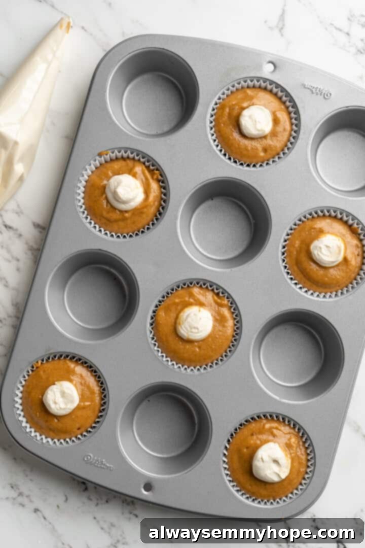 These vegan pumpkin cream cheese muffins pair the cozy flavour of pumpkin with a sweet-and-tangy cream cheese filling with delicious results! Overhead view of cream cheese filling being piped into the center of muffin batter in a pan, creating a swirl.