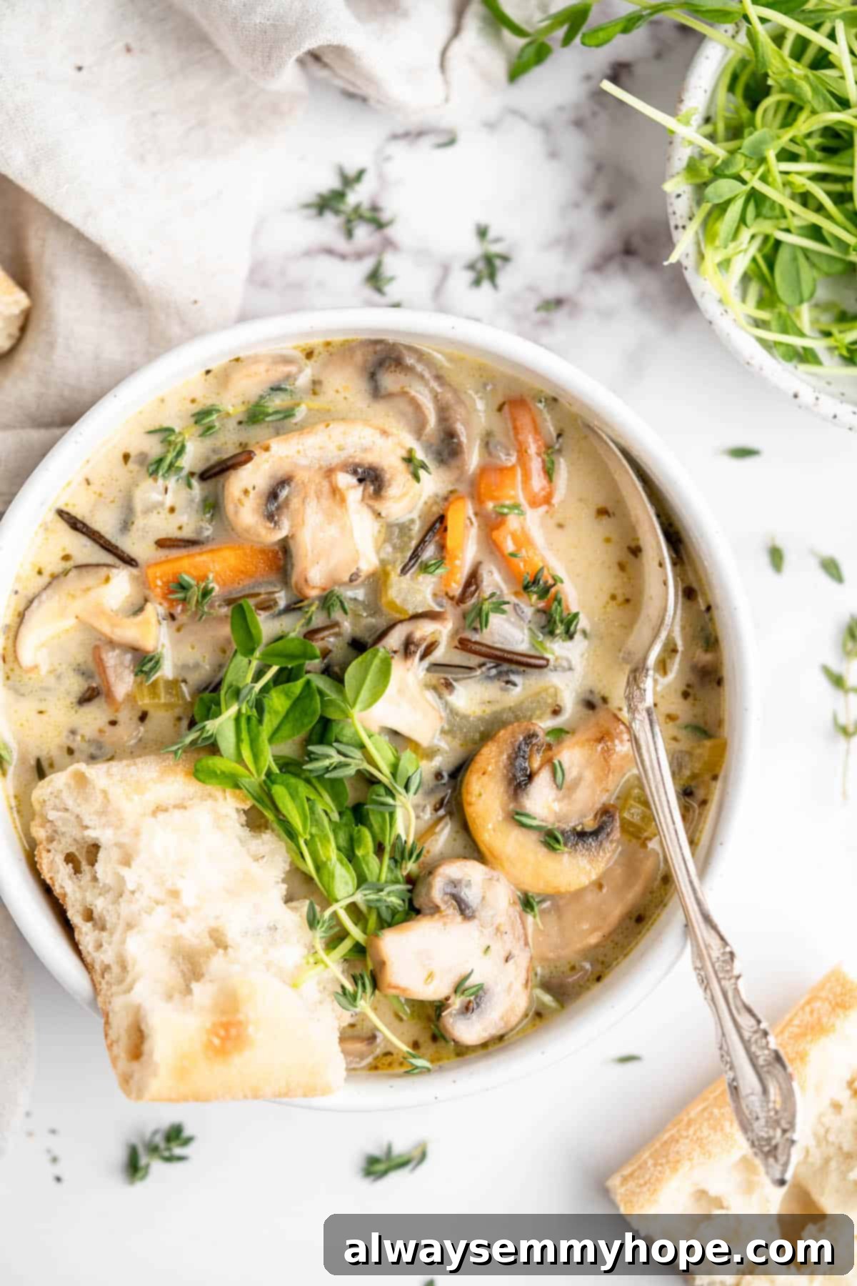 Velvety Vegan Mushroom Wild Rice Soup 2 A steaming bowl of creamy vegan mushroom wild rice soup, garnished with fresh herbs, alongside a slice of crusty bread and a spoon. The earthy tones of mushrooms and wild rice are visible in the rich, hearty broth.