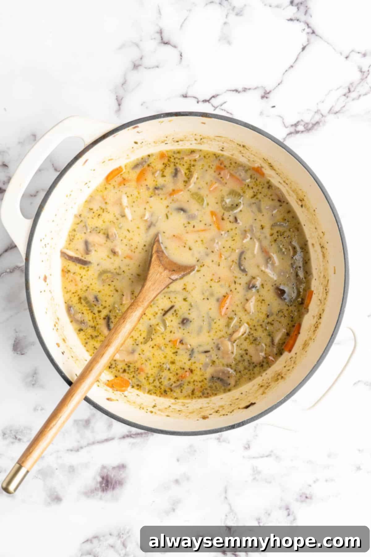 Velvety Vegan Mushroom Wild Rice Soup 7 Overhead view of a pot filled with finished creamy vegan mushroom wild rice soup, ready to be served, with a wooden spoon resting inside.