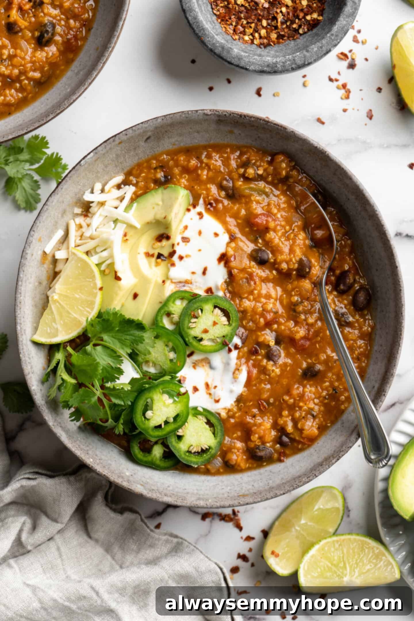 Close up of a vibrant bowl of Vegan Pumpkin Chili, generously topped with fresh avocado slices and thinly sliced jalapeños.