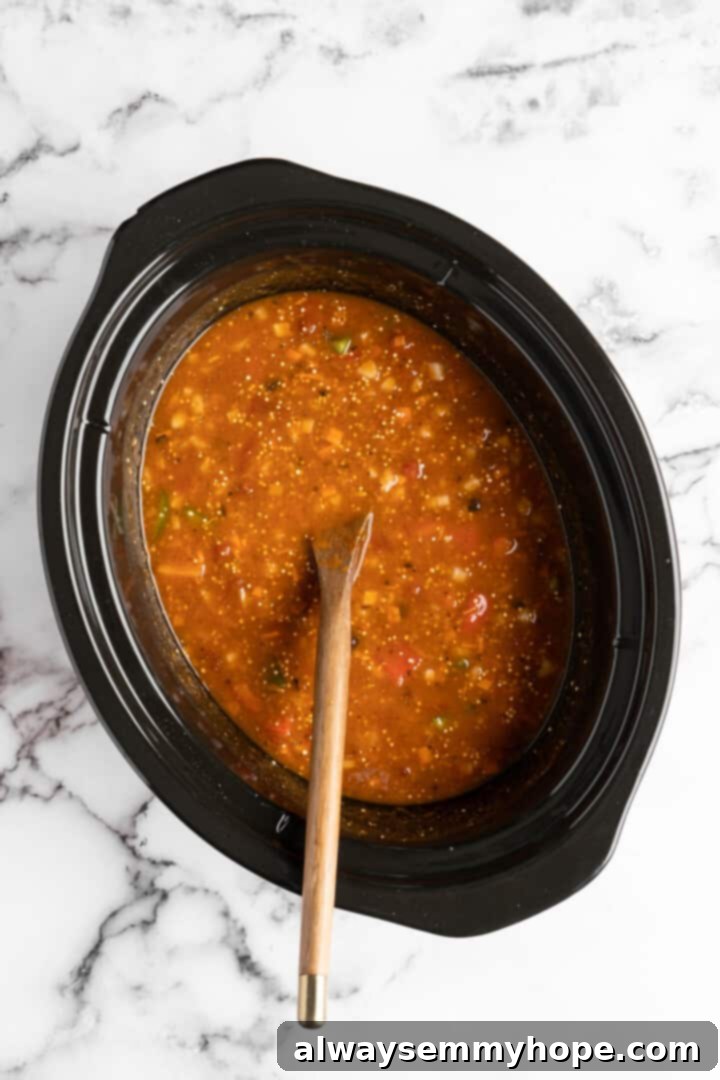 The vegan pumpkin chili simmering in the slow cooker, showing the rich texture and vibrant colors of the ingredients as it cooks.
