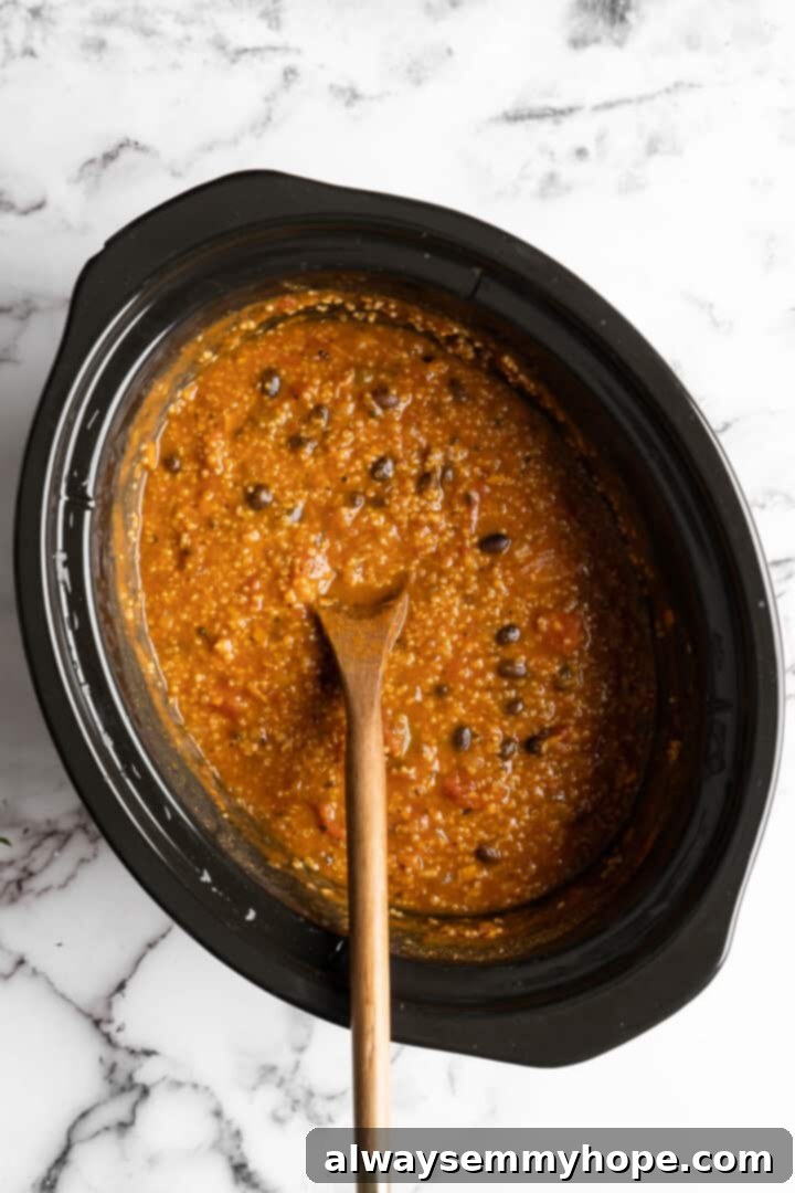 A close-up view of the finished vegan pumpkin chili in the slow cooker, thick and ready to be served, showcasing the chunky vegetables and beans.