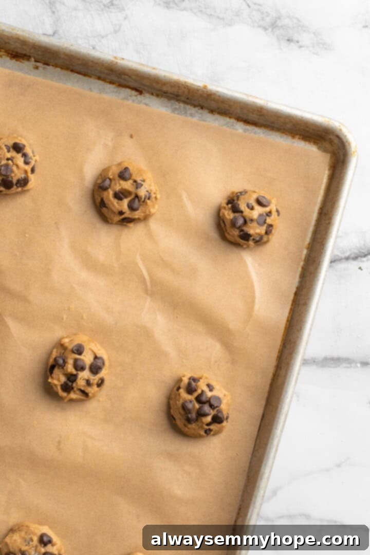 Decadent Chewy Salted Tahini Chocolate Chip Cookies 6 Scooped and rolled cookie dough balls placed on a baking sheet, ready for the oven.