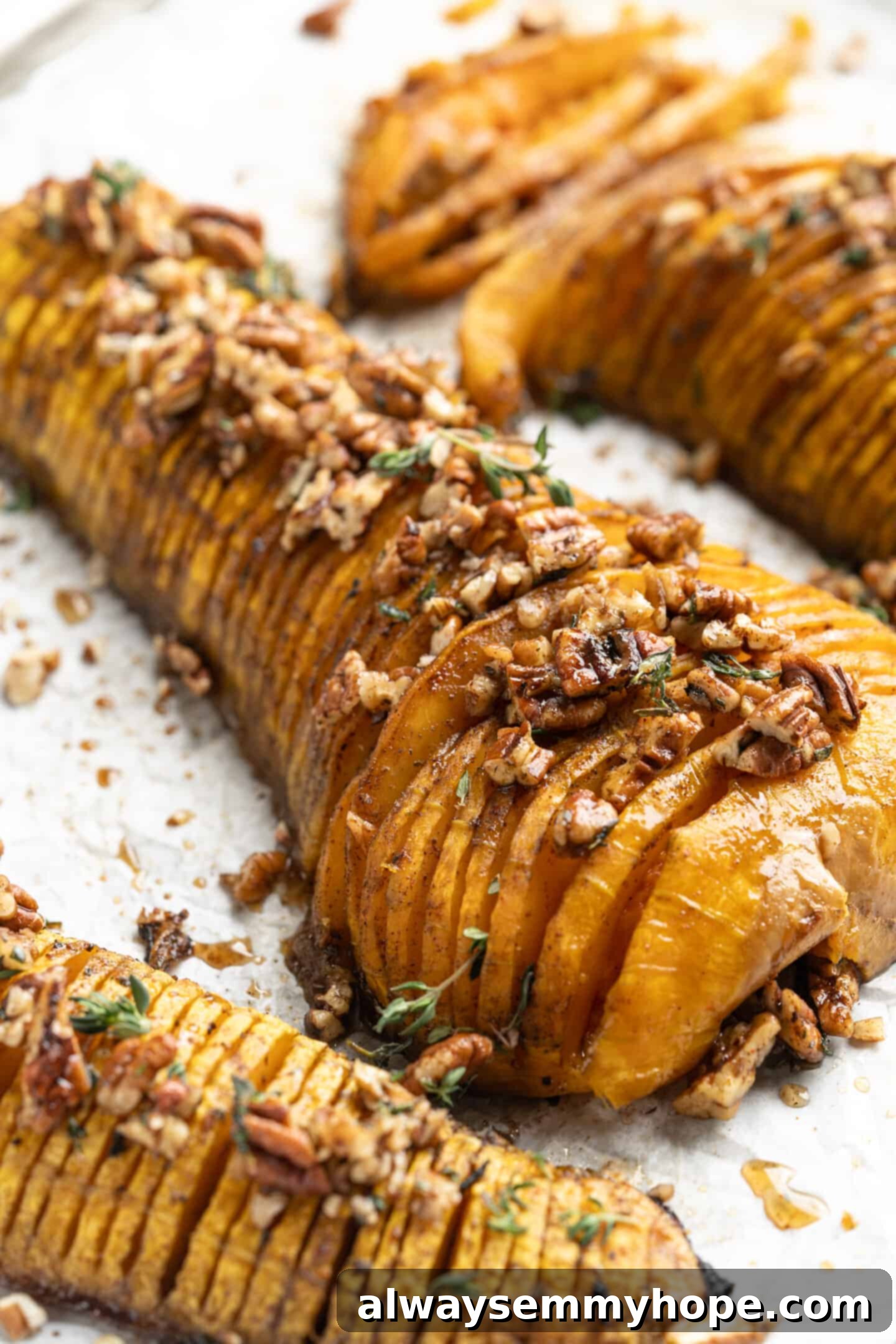 Hasselback butternut squash is a show-stopper, but it’s not all looks! Maple, tender squash, and caramelised pecans make it irresistible! Hasselback butternut squash with maple glazed pecans and thyme arranged beautifully on a serving dish, ready for a holiday meal