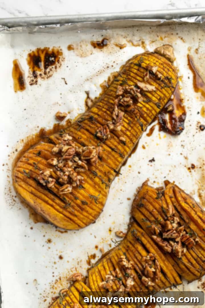 Hasselback butternut squash is a show-stopper, but it’s not all looks! Maple, tender squash, and caramelised pecans make it irresistible! Hasselback butternut squash on a parchment-lined baking sheet, prepared with glaze and thyme, ready for its final bake