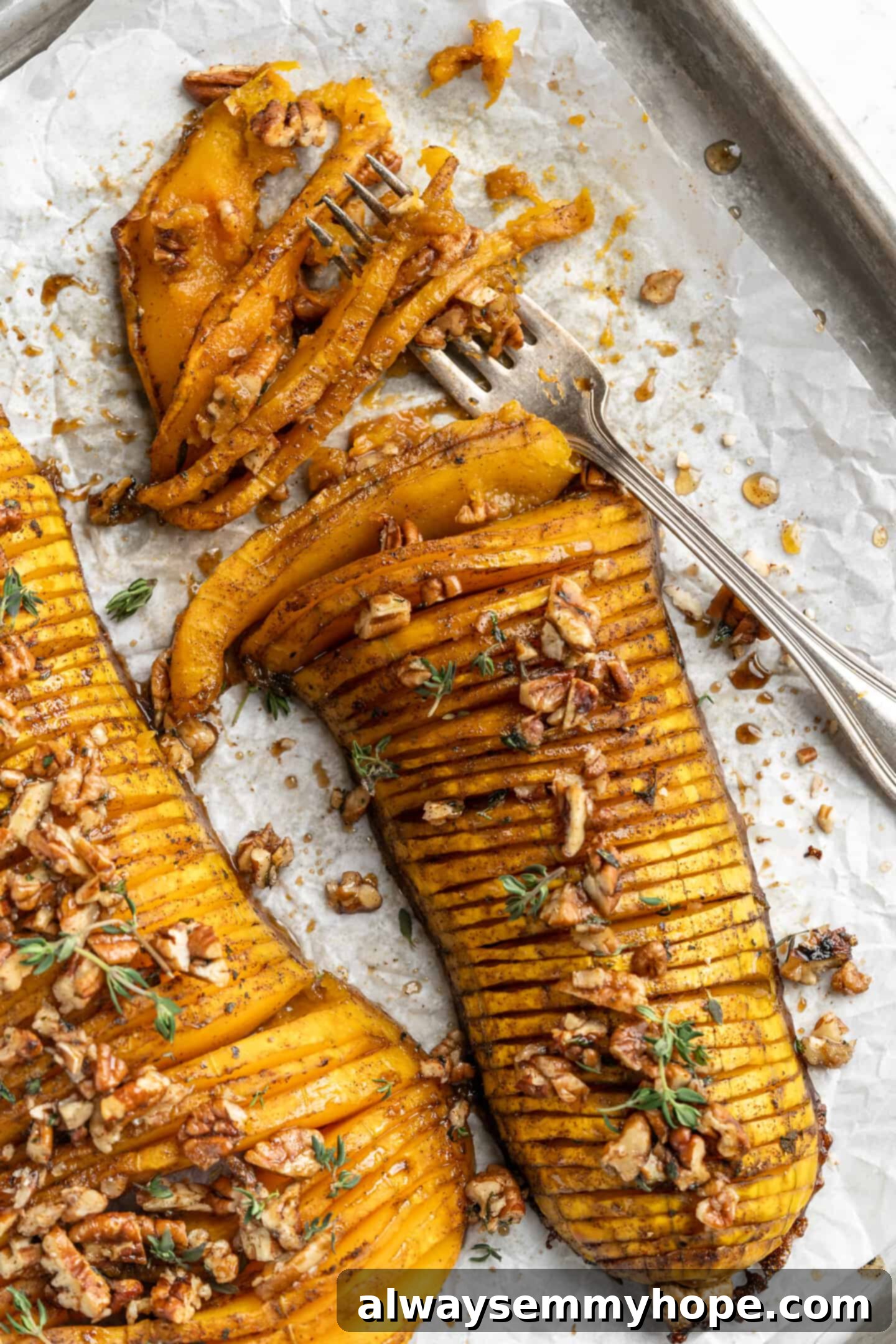 Hasselback butternut squash is a show-stopper, but it’s not all looks! Maple, tender squash, and caramelised pecans make it irresistible! Overhead view of a cooked Hasselback butternut squash on a serving plate with a fork, showing its tender, fanned slices