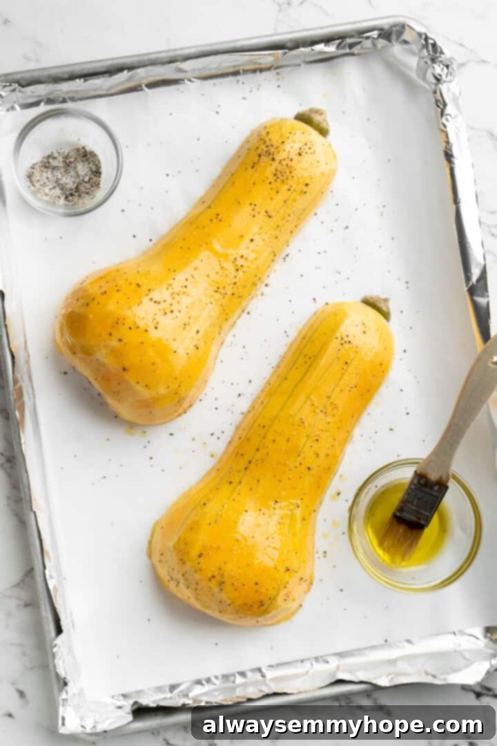 Hasselback butternut squash is a show-stopper, but it’s not all looks! Maple, tender squash, and caramelised pecans make it irresistible! Overhead view of butternut squash halves seasoned with oil, salt, and pepper on a parchment-lined baking pan, ready for roasting