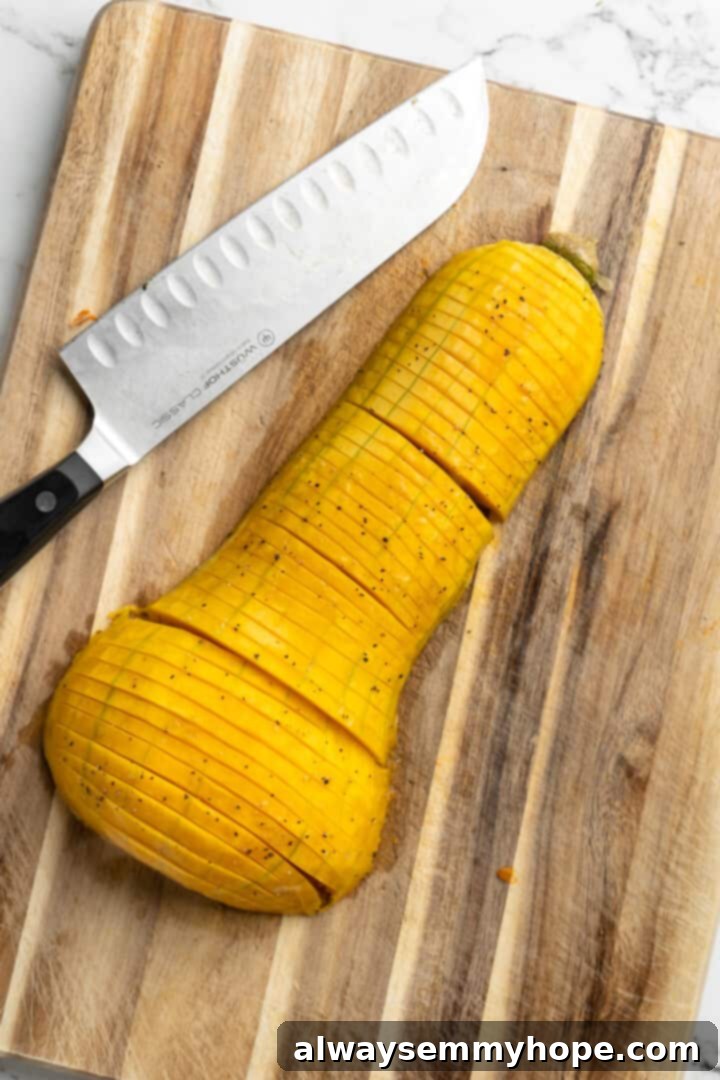 Hasselback butternut squash is a show-stopper, but it’s not all looks! Maple, tender squash, and caramelised pecans make it irresistible! Overhead view of a butternut squash half on a cutting board, with a knife making precise hasselback slits
