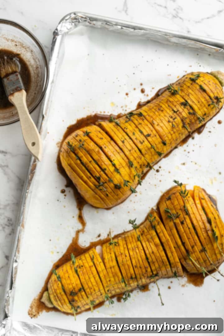Hasselback butternut squash is a show-stopper, but it’s not all looks! Maple, tender squash, and caramelised pecans make it irresistible! Hasselback butternut squash on a pan, beautifully fanned out and glistening after the maple glaze has been brushed on