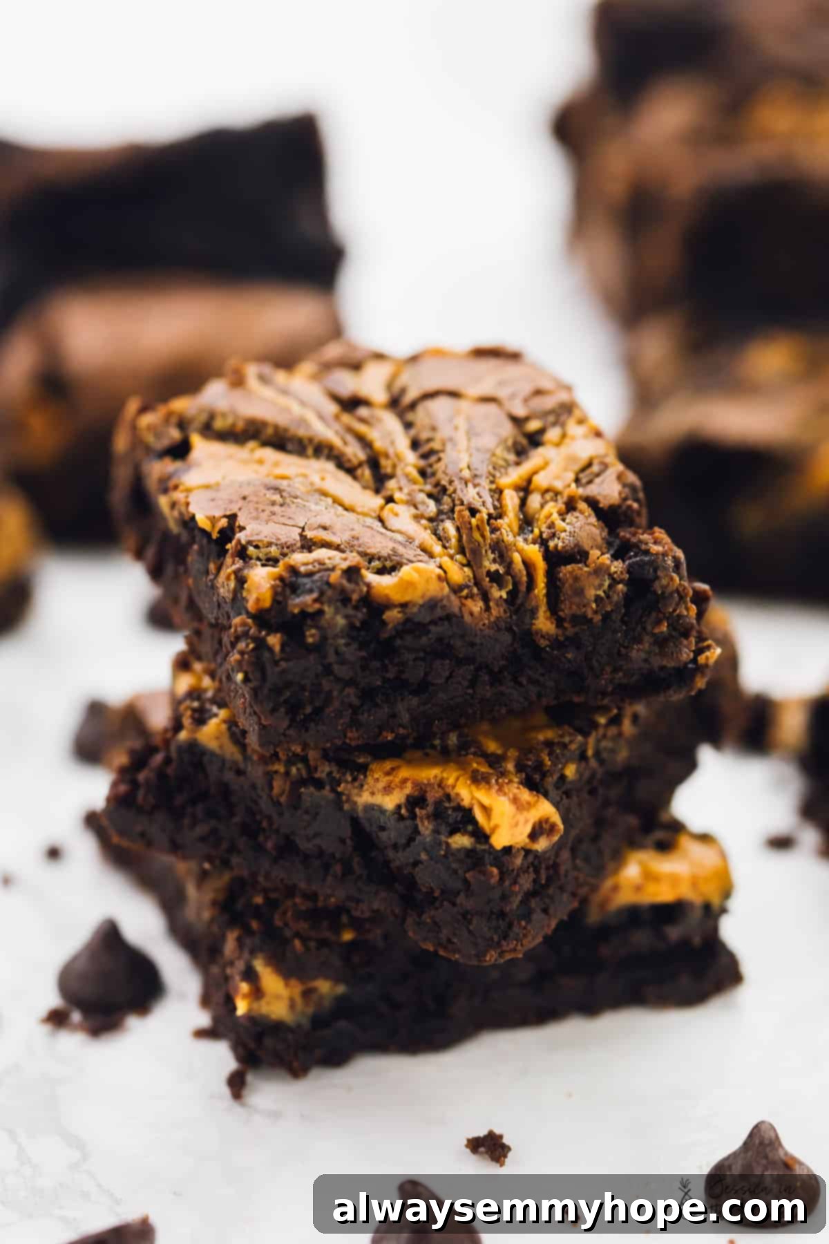A stack of vegan chocolate peanut butter swirl brownies, surrounded by chocolate chips. 