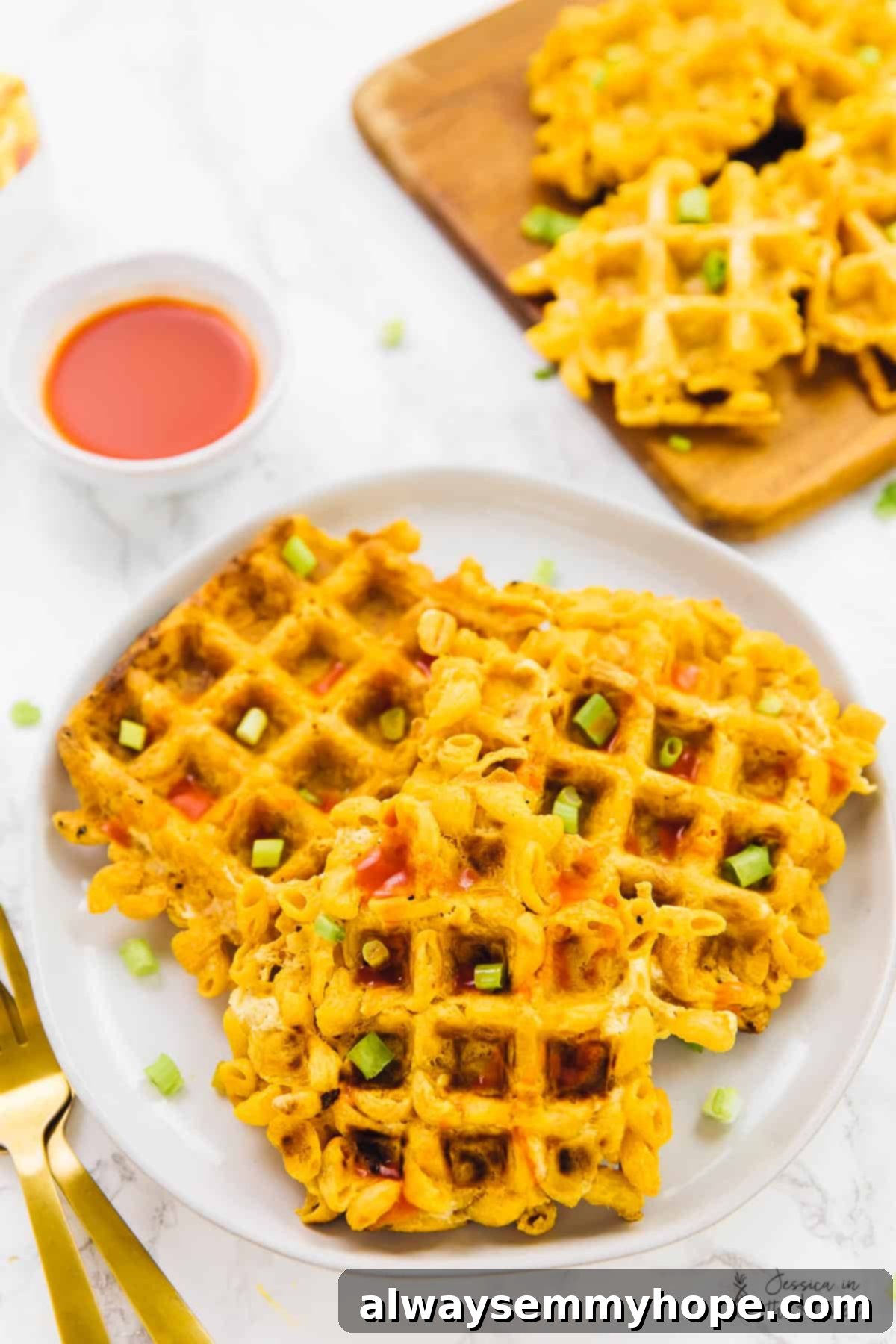 Top down view of crispy mac and cheese waffles on a plate with sauce on the side.