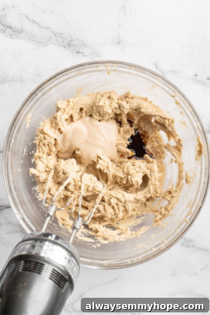 Overhead view of a stand mixer beating wet ingredients in a large mixing bowl, creating a creamy mixture.
