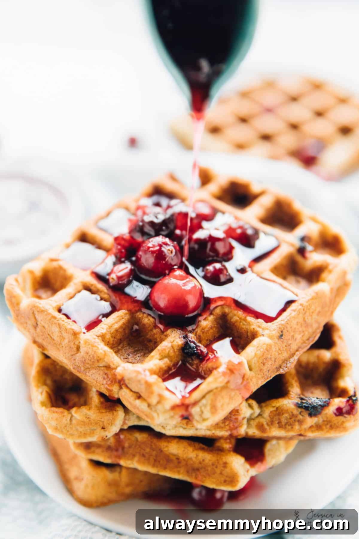 Syrup being generously poured onto a luscious stack of golden orange cranberry waffles, highlighting their delicious and festive appeal.