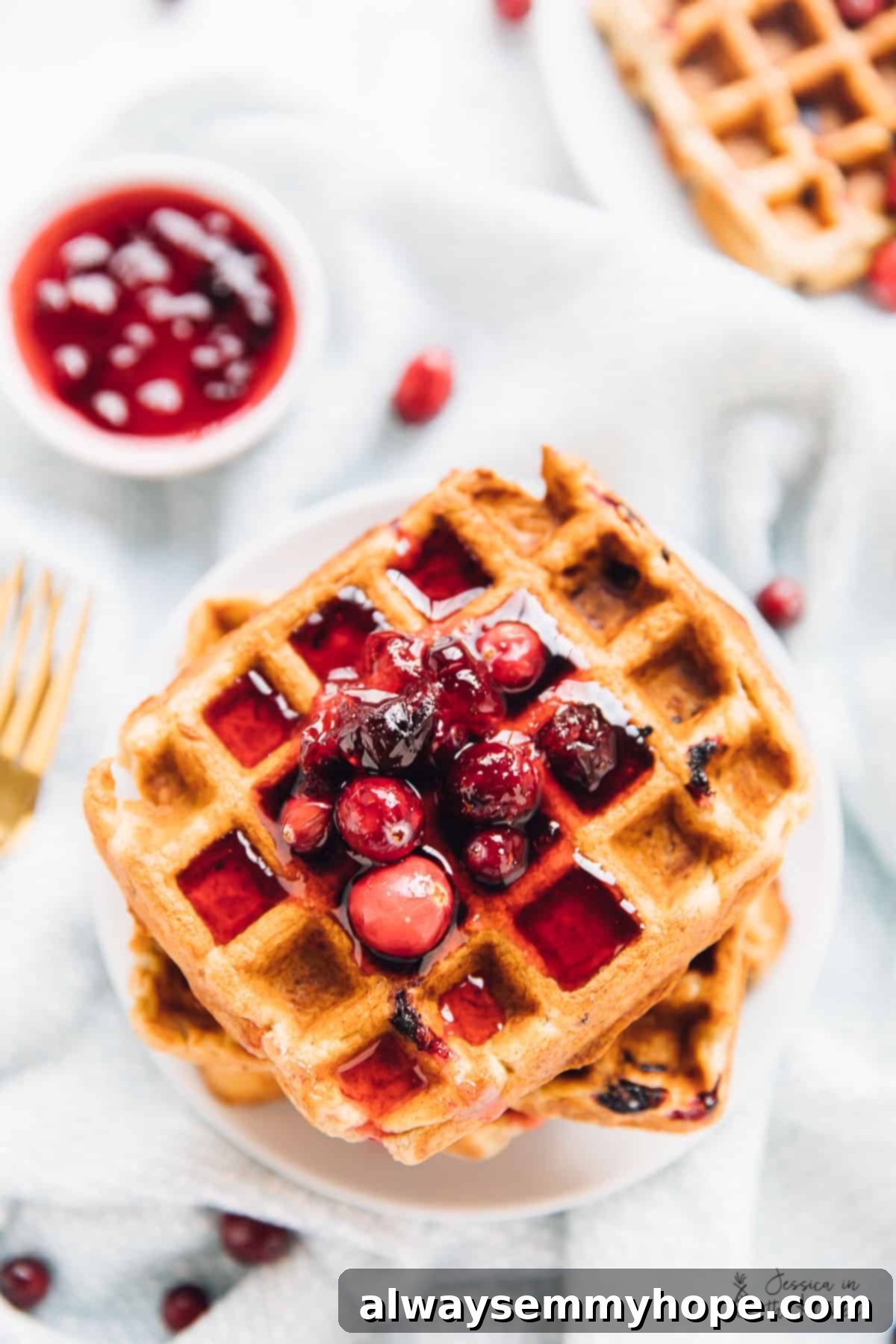 A vibrant top-down shot of golden orange cranberry waffles, lavishly drizzled with a homemade cranberry maple compote, perfect for a festive breakfast.