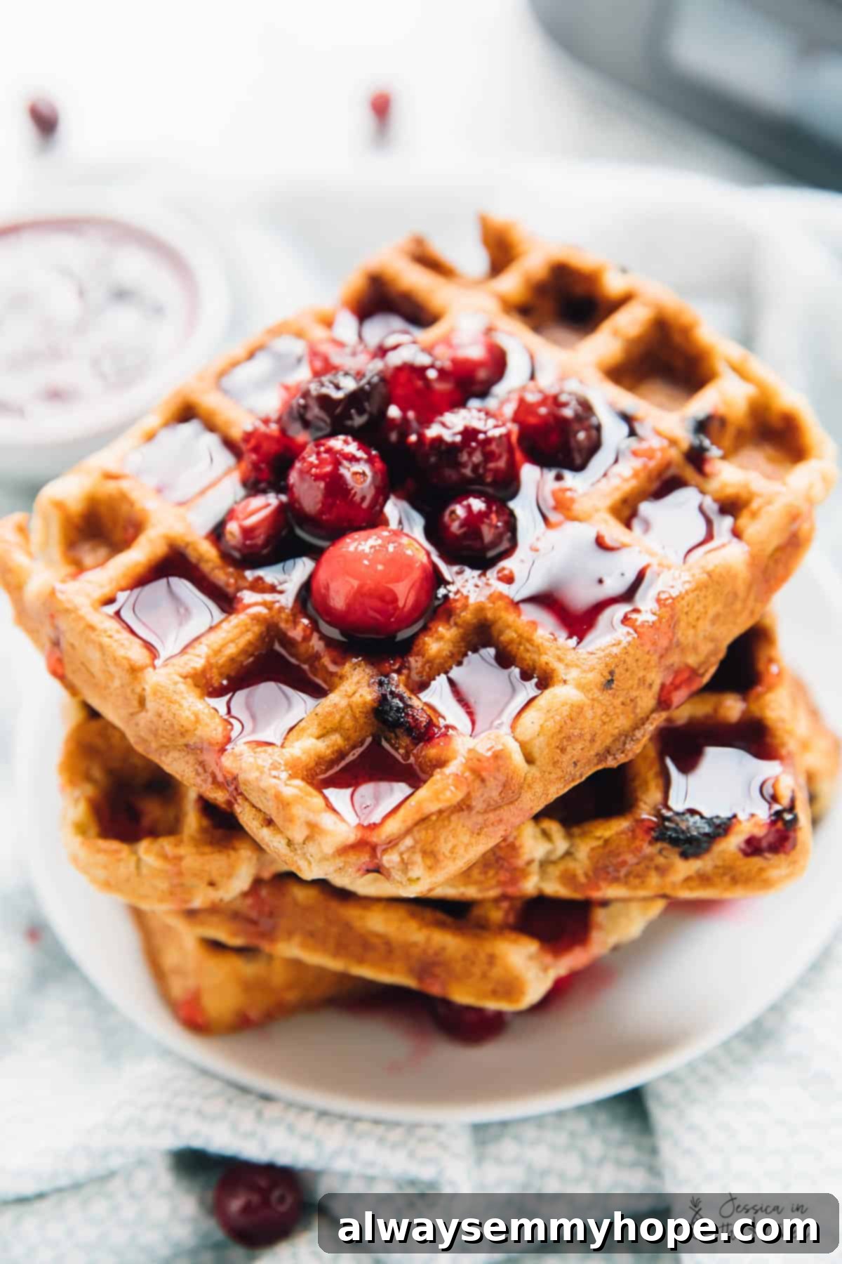 A perfectly stacked set of four golden-brown orange cranberry waffles, invitingly covered in sweet maple syrup.