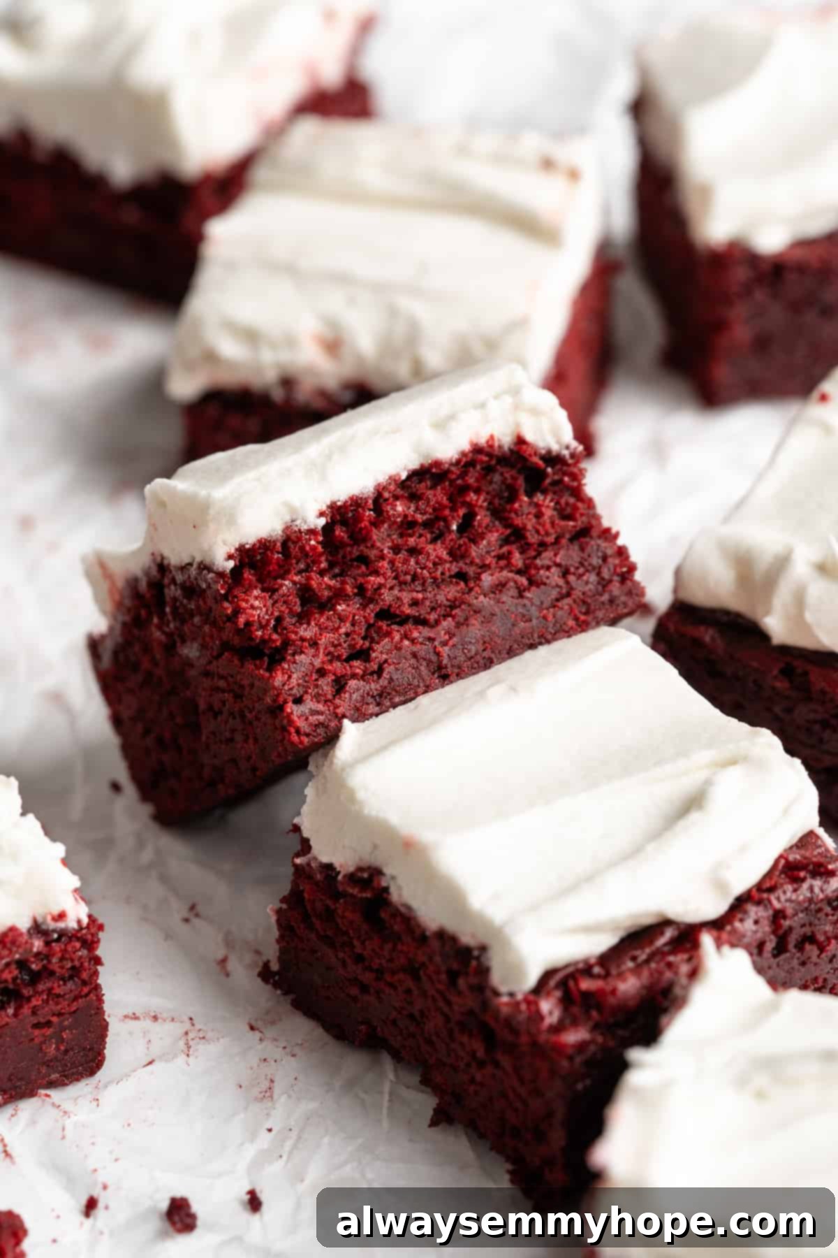 Moist, rich red velvet brownies are perfect for a special occasion or anytime you’re craving a decadent dessert. With cream cheese frosting! Moist and rich vegan red velvet brownies on parchment paper, with one brownie tipped sideways to show its perfect, fudgy crumb texture, topped with fluffy cream cheese frosting.