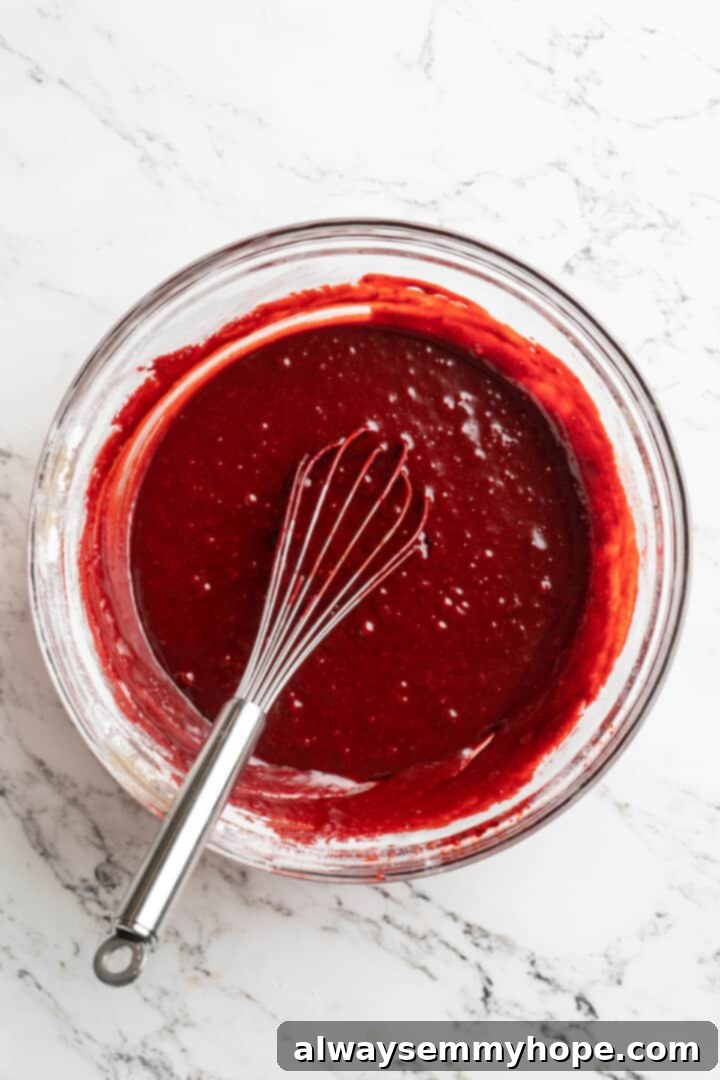 Moist, rich red velvet brownies are perfect for a special occasion or anytime you’re craving a decadent dessert. With cream cheese frosting! Overhead view of vibrant red velvet brownie batter in a mixing bowl, showing its smooth, rich consistency, with a whisk resting in it.