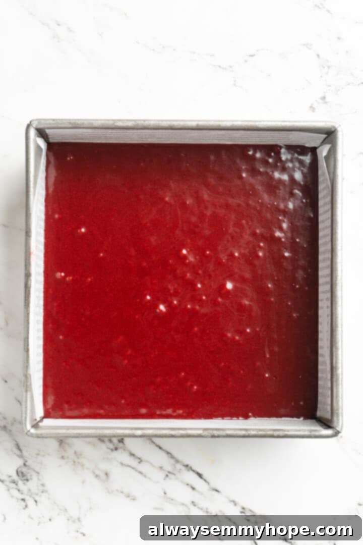 Moist, rich red velvet brownies are perfect for a special occasion or anytime you’re craving a decadent dessert. With cream cheese frosting! Overhead view of smooth, vibrant red velvet brownie batter evenly spread in a parchment-lined square baking pan, ready for the oven.