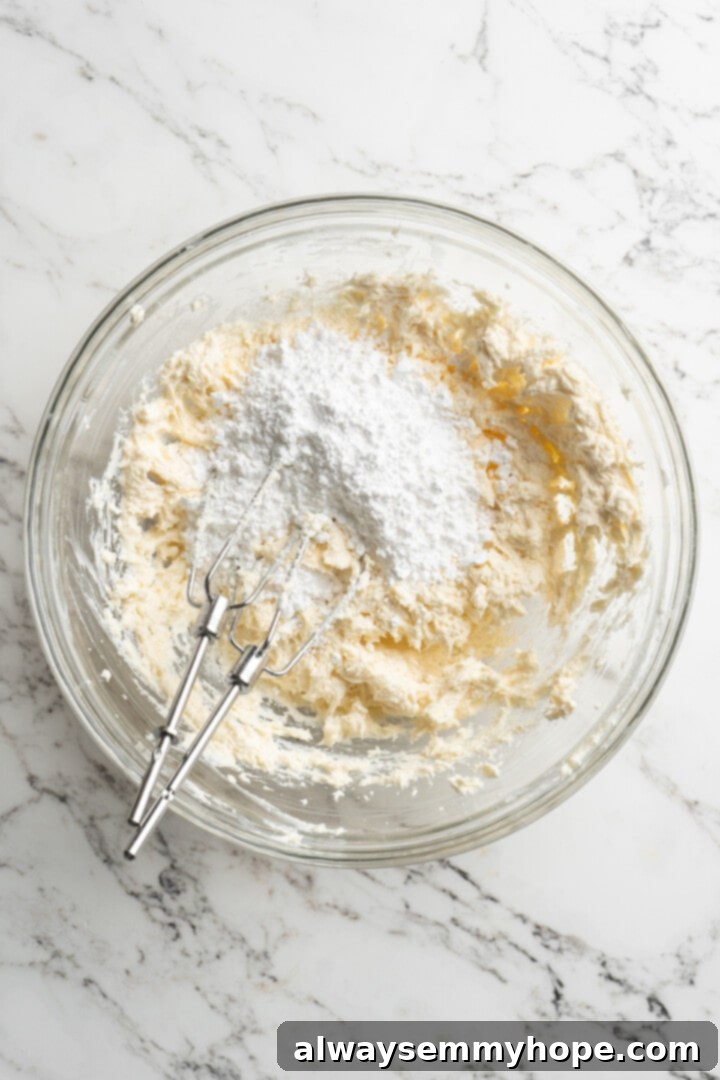 Moist, rich red velvet brownies are perfect for a special occasion or anytime you’re craving a decadent dessert. With cream cheese frosting! Overhead view of sifted powdered sugar being added to a mixing bowl containing creamed vegan butter and cream cheese, ready to be incorporated into frosting.