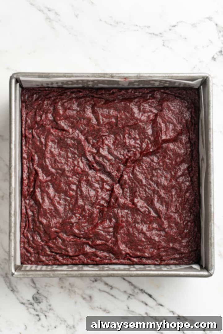 Moist, rich red velvet brownies are perfect for a special occasion or anytime you’re craving a decadent dessert. With cream cheese frosting! Overhead view of freshly baked vegan red velvet brownies cooling in a square pan lined with parchment paper.