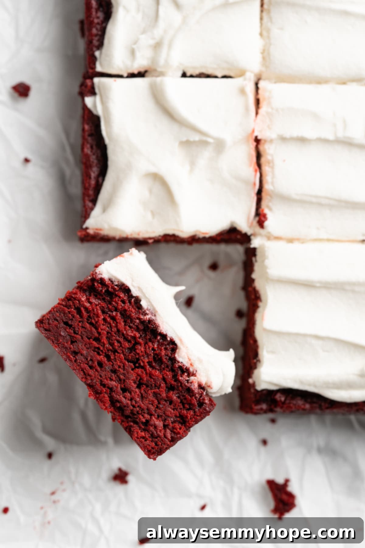 Moist, rich red velvet brownies are perfect for a special occasion or anytime you’re craving a decadent dessert. With cream cheese frosting! A close-up shot of several vegan red velvet brownies on parchment paper, with one brownie tipped sideways to show its moist, vibrant red crumb, all topped with a generous layer of white cream cheese frosting.