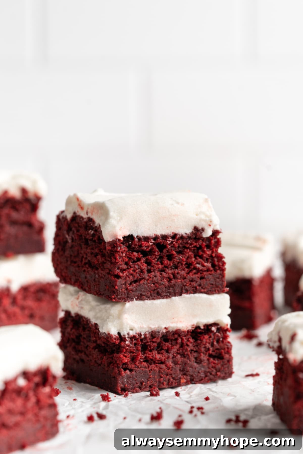 Moist, rich red velvet brownies are perfect for a special occasion or anytime you’re craving a decadent dessert. With cream cheese frosting! Two perfectly stacked vegan red velvet brownies, generously frosted with creamy white cream cheese frosting, resting on parchment paper.
