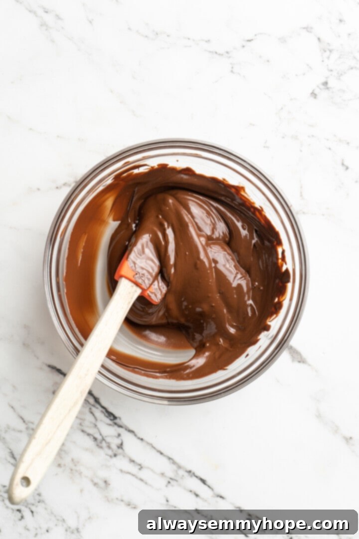 Moist, rich red velvet brownies are perfect for a special occasion or anytime you’re craving a decadent dessert. With cream cheese frosting! Overhead view of glistening melted vegan chocolate chips in a clear glass bowl, with a silicone spatula resting inside.