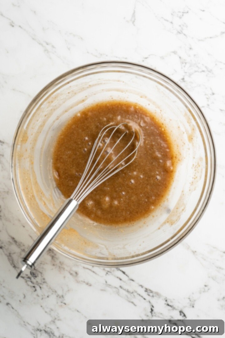 Moist, rich red velvet brownies are perfect for a special occasion or anytime you’re craving a decadent dessert. With cream cheese frosting! Overhead view of brown sugar, oil, and flax egg mixture being whisked together in a clear glass bowl, creating a smooth, emulsified texture.