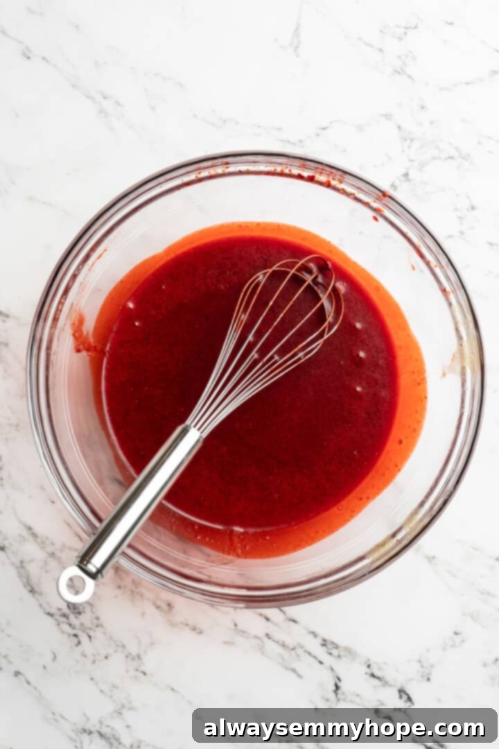 Moist, rich red velvet brownies are perfect for a special occasion or anytime you’re craving a decadent dessert. With cream cheese frosting! Overhead view of liquid ingredients for red velvet brownies – water, vanilla extract, and natural red food coloring – mixed into the sugar, oil, and flax egg base in a glass bowl with a whisk.