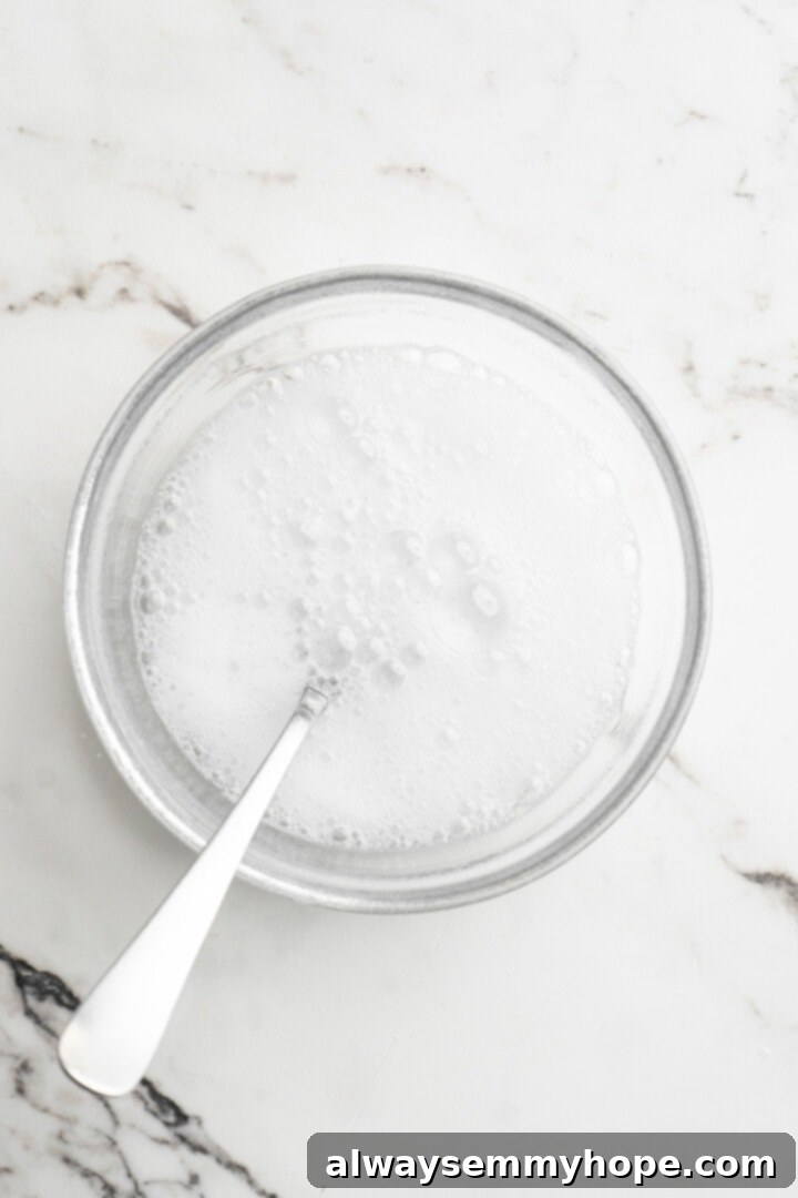 Moist, rich red velvet brownies are perfect for a special occasion or anytime you’re craving a decadent dessert. With cream cheese frosting! Overhead view of vinegar and baking soda mixture fizzing in a small bowl, with a spoon inside.