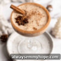 Creamy Heartwarming Vegan Eggnog 2 A cocktail glass on a plate filled with vegan eggnog, garnished with a cinnamon stick, a star anise pod, and ground cinnamon, with a cinnamon sugar rim