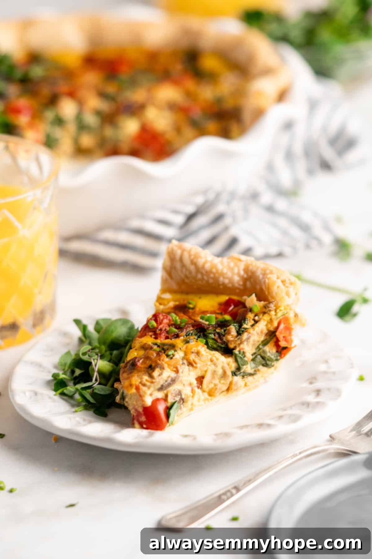 Slice of vegan quiche on a plate with fresh greens, accompanied by a glass of orange juice in the background, highlighting its deliciousness and perfect texture.