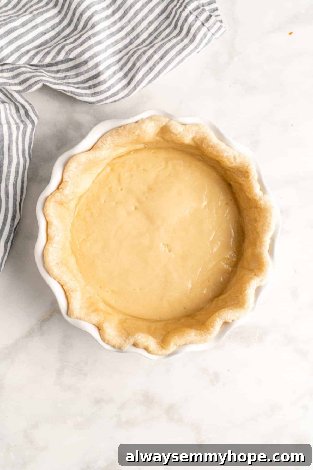 An overhead view of a perfectly shaped pie crust nestled in a baking dish, lightly floured and ready for pre-baking, setting the stage for a delicious quiche.