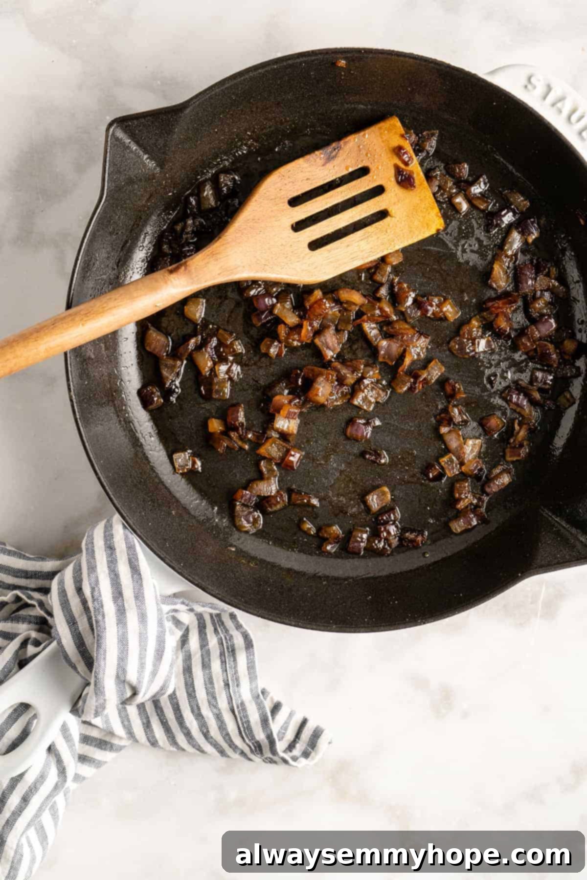 An overhead view of finely sliced red onions gently caramelizing in a cast iron skillet, showcasing their rich, golden-brown color and sweet aroma developing as they cook.
