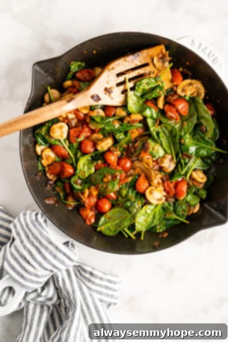 A close-up, overhead shot of a medley of vegetables including tomatoes, mushrooms, and spinach, perfectly sautéed in a cast iron skillet, vibrant and ready for the quiche filling.