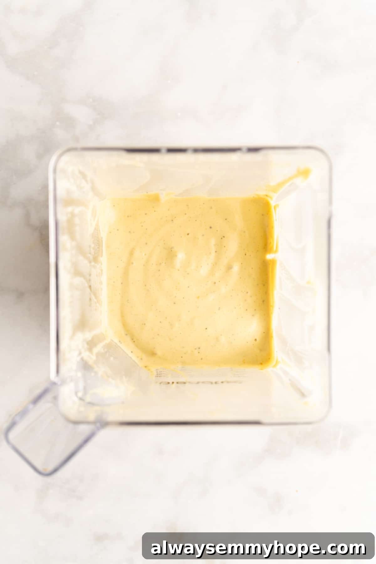 An overhead shot of a creamy, pale yellow tofu quiche filling being blended in a high-powered blender, showcasing its smooth consistency before being added to the crust.