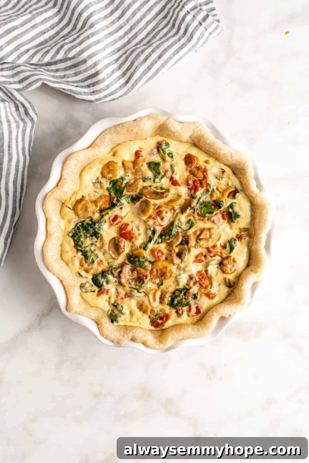 An overhead view of the assembled vegan quiche before baking, with the creamy tofu filling poured over a bed of colorful sautéed vegetables in a pie crust, ready for the oven.