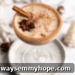 A cocktail glass on a plate filled with vegan eggnog, garnished with a cinnamon stick, a star anise pod, and ground cinnamon, with a cinnamon sugar rim