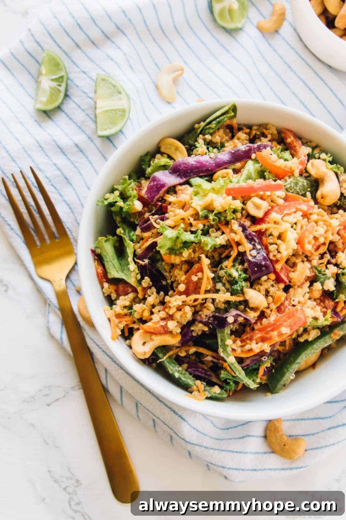 17 Smart Meal Prep Salads to Kickstart Your New Year 12 Top-down view of a vibrant cashew Thai quinoa salad in a white bowl, adorned with a shining gold fork, showcasing its rich textures and luscious peanut ginger sauce.