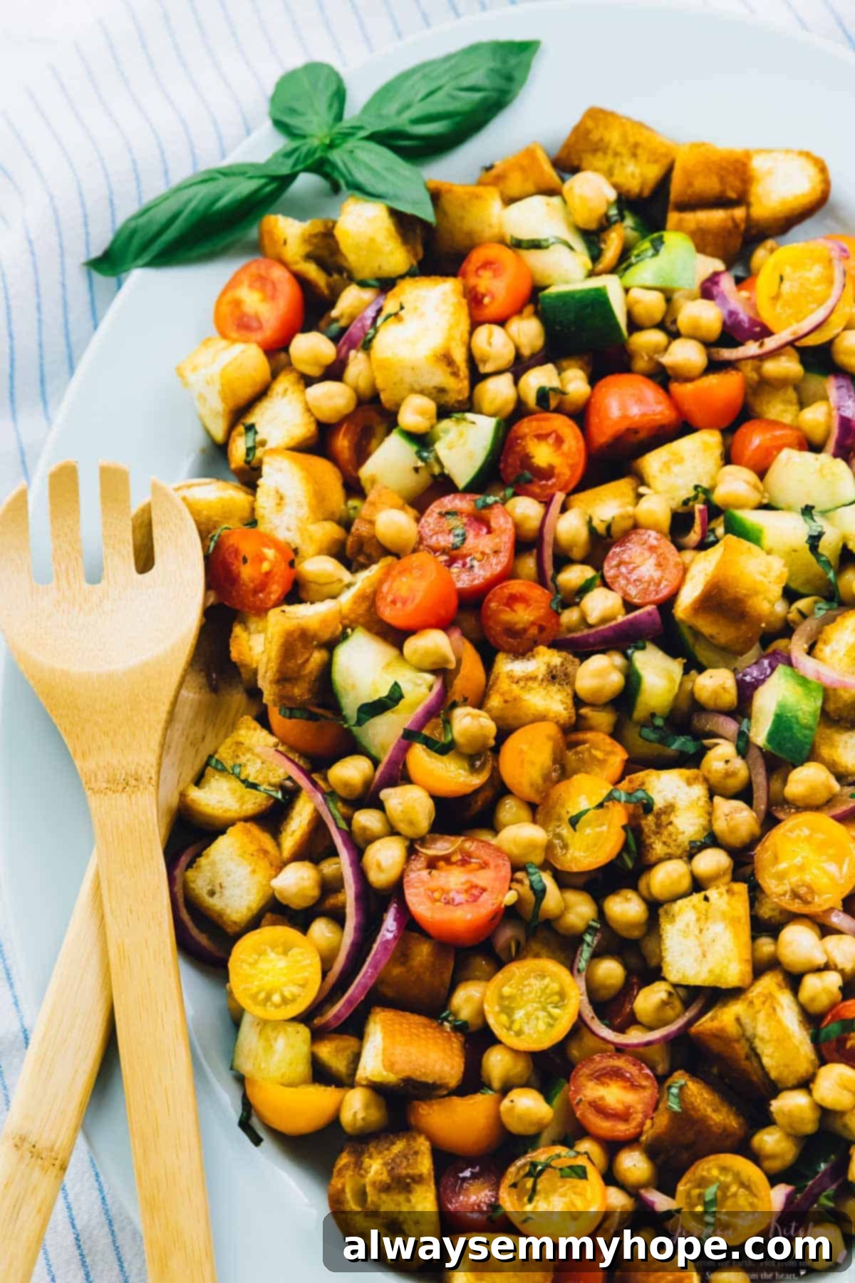 17 Smart Meal Prep Salads to Kickstart Your New Year 13 Overhead view of a rustic and inviting chickpea panzanella salad, featuring crusty bread, fresh garden vegetables, and hearty chickpeas, with a spork resting on the side.
