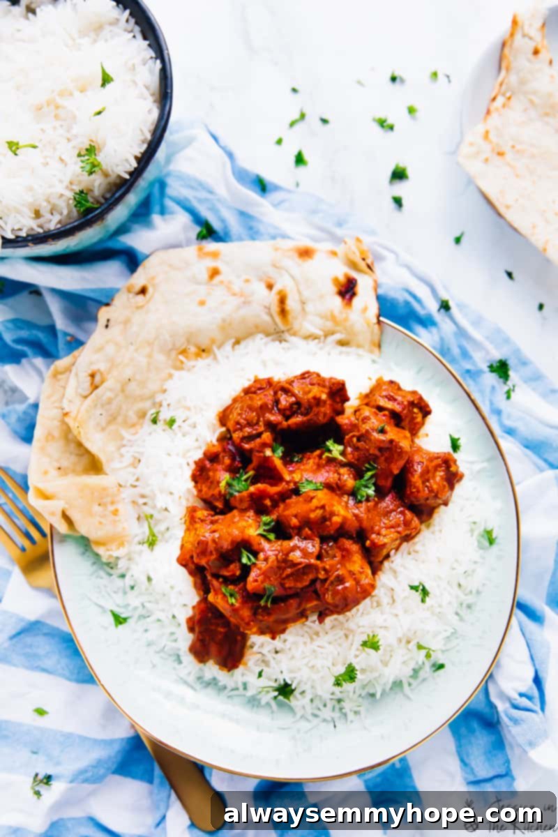 An overhead shot of a vegan slow cooker tofu butter 'chicken' dish with rice and naan Top down view of Slow Cooker Tofu Butter Chicken on a bed of rice with fluffy naan bread on the side. The dish is rich, creamy, and garnished with fresh cilantro.