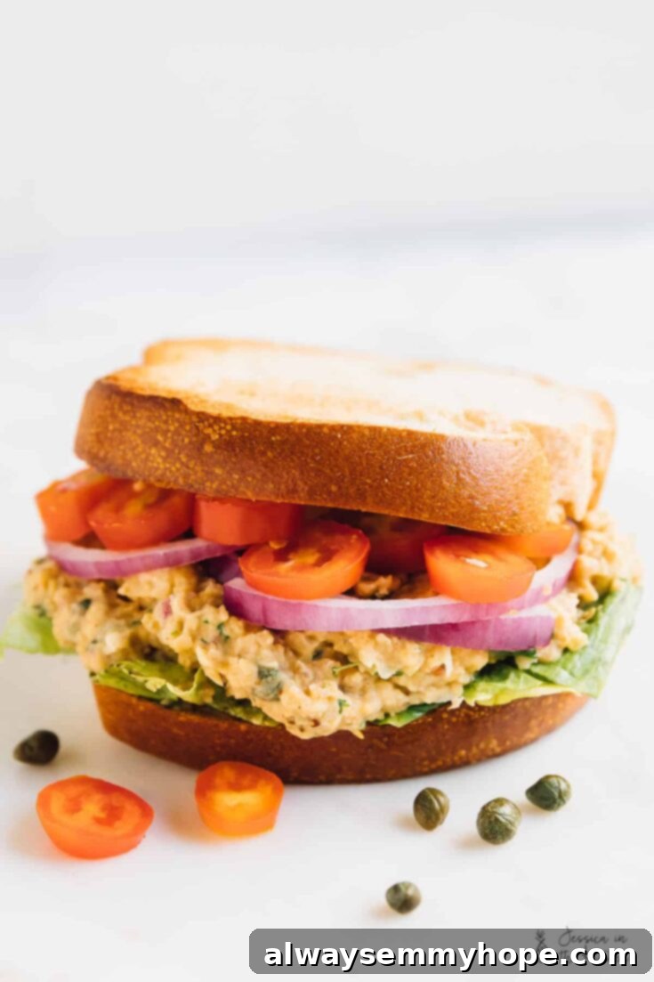 A delicious vegan tuna sandwich made with mashed chickpeas, served on whole wheat bread with fresh greens and tomato slices.