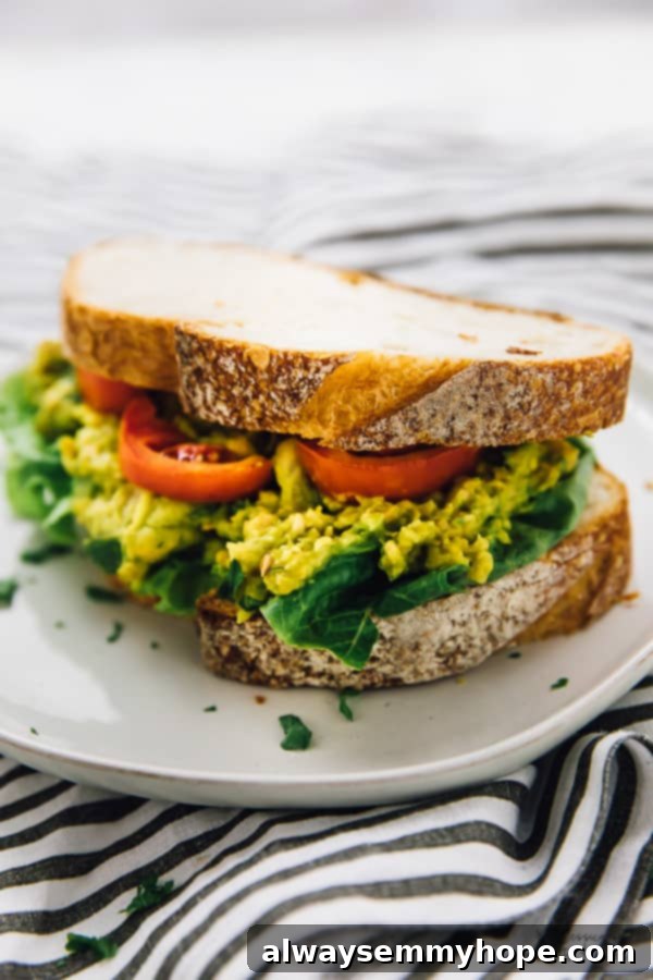 A vibrant smashed chickpea and avocado sandwich on toasted bread, garnished with fresh herbs and a hint of lime.