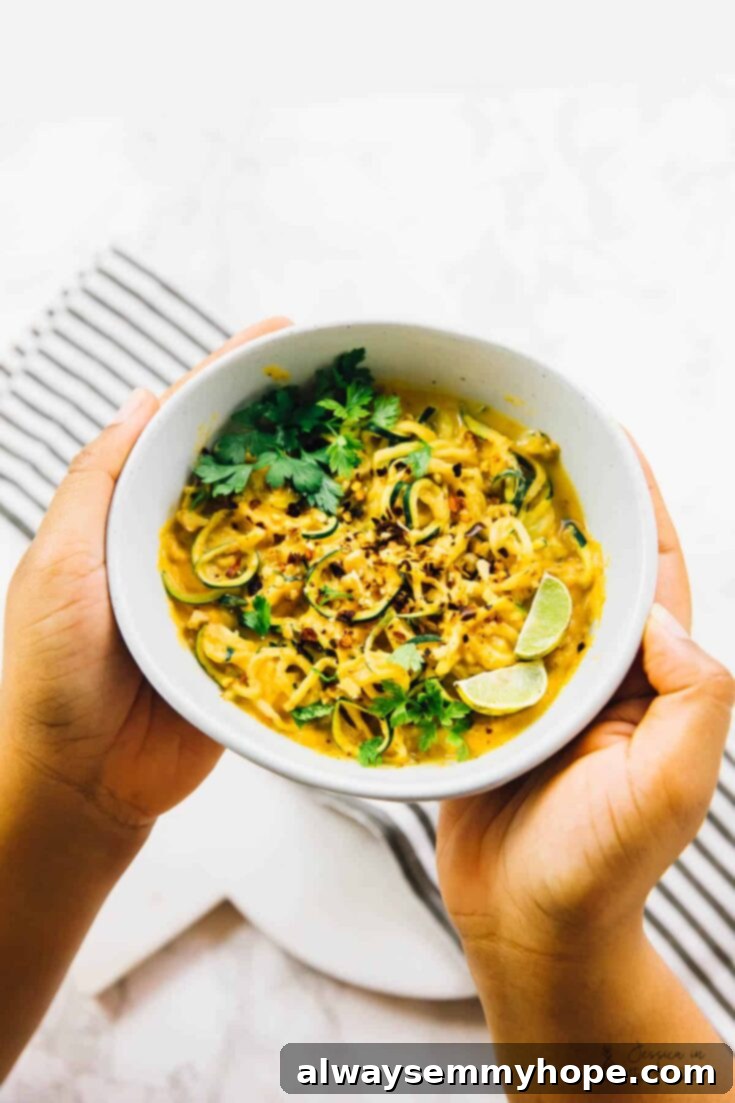 A colorful bowl of curried satay veggies, generously coated in a creamy chickpea-based sauce, garnished with fresh cilantro and crushed peanuts.