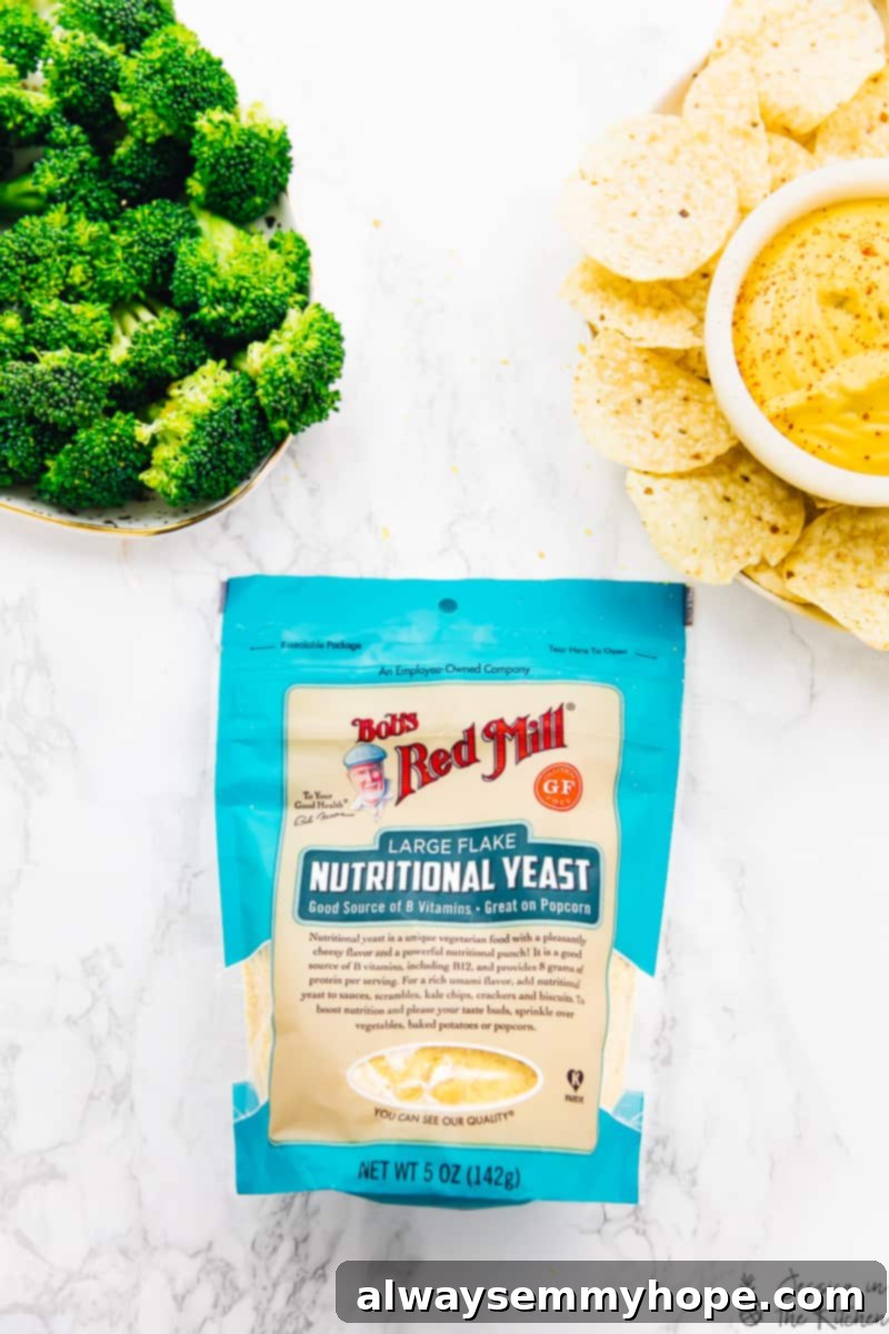 A bag of Bob's Red Mill nutritional yeast positioned next to a beautifully arranged platter of vegan cheese sauce, crispy tortilla chips, and fresh broccoli florets, emphasizing healthy and delicious snacking.